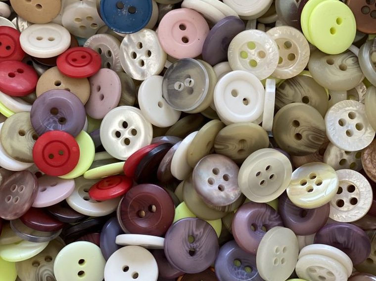 A close packed tray of buttons in cream, red, olive, mauve and mother-of-pearl.