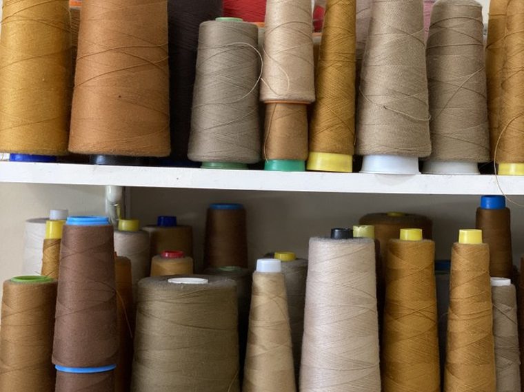 Two shelves of large thread cones in tan, brown and khaki.